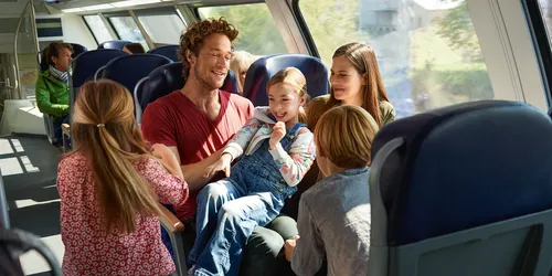 Happy family enjoying a scenic train journey together, parents and children looking out the window